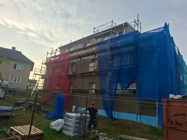 Bytový dům v Ločenicích během prací na fasádě, lešení se sítěmi a materiál na stavbě