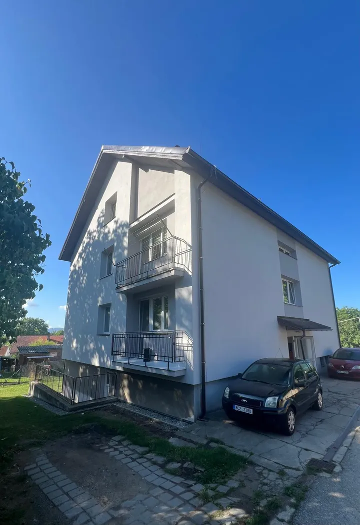 Bytový dům v Otěvěku po rekonstrukci, roh s balkony, nová světlá fasáda a nová střecha