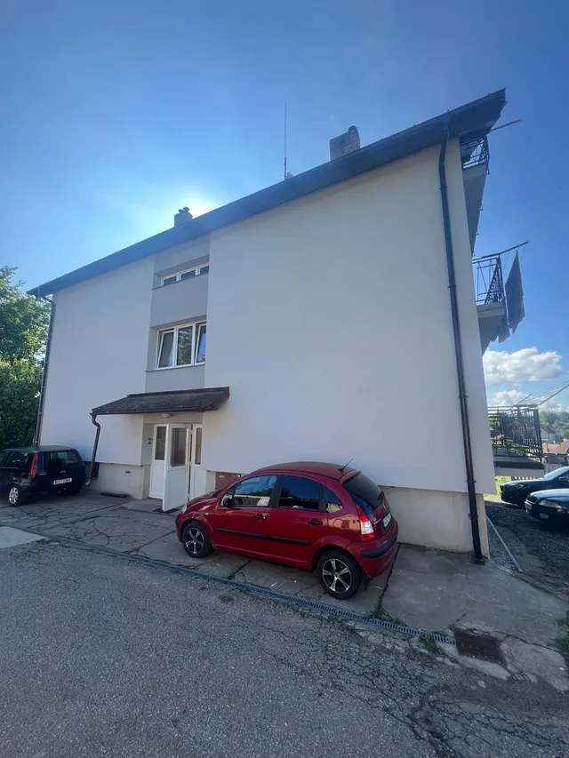 Vstupní strana bytového domu v Otěvěku s novou fasádou a šedým pásem kolem oken schodiště